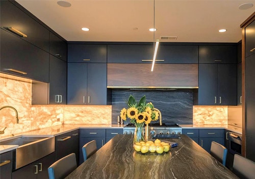 Kitchen remodel project Cleveland Ohio - Sunflowers and lemons on the table with modern lighting under the dark cabinets, can lights, modern led light fixture, and glowing marble backsplash.