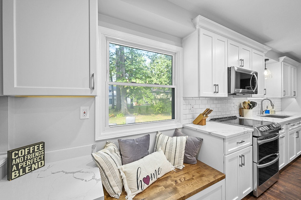 A kitchen window seat featuring natural wood grain, under a large and bright window