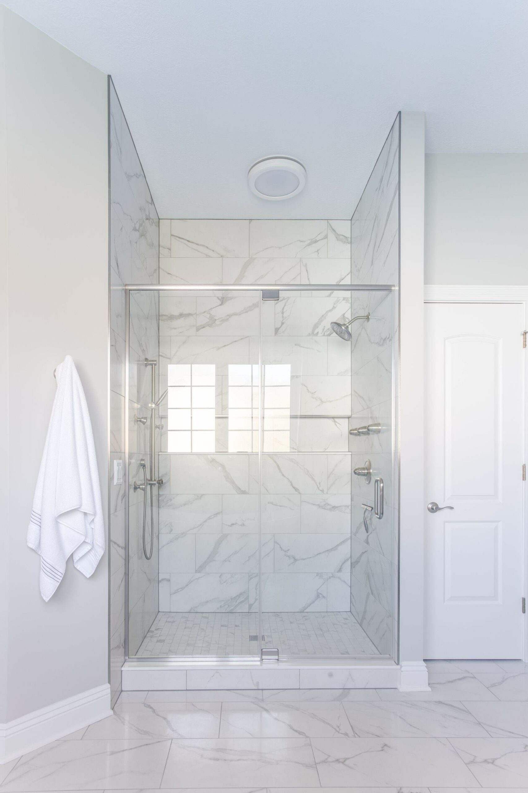 A light and airy bathroom after renovation, featuring white marble tiles on bathroom floor and shower walls. A glass shower door adds a sense of space