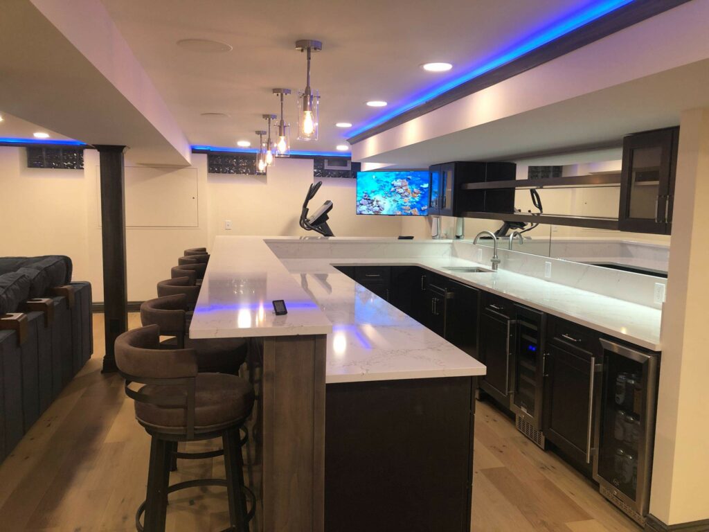 A wet bar in a refinished basement, with marble countertops and bar stools
