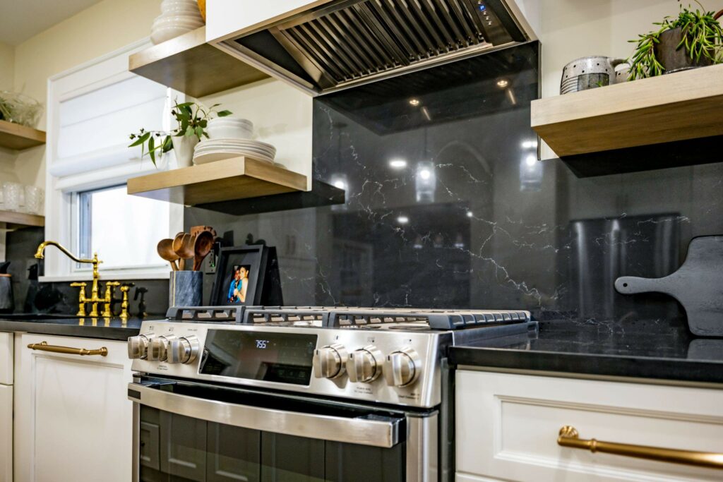 A sleek, modern stove and range. Featuring floating wood shelves and a shiny black backsplash
