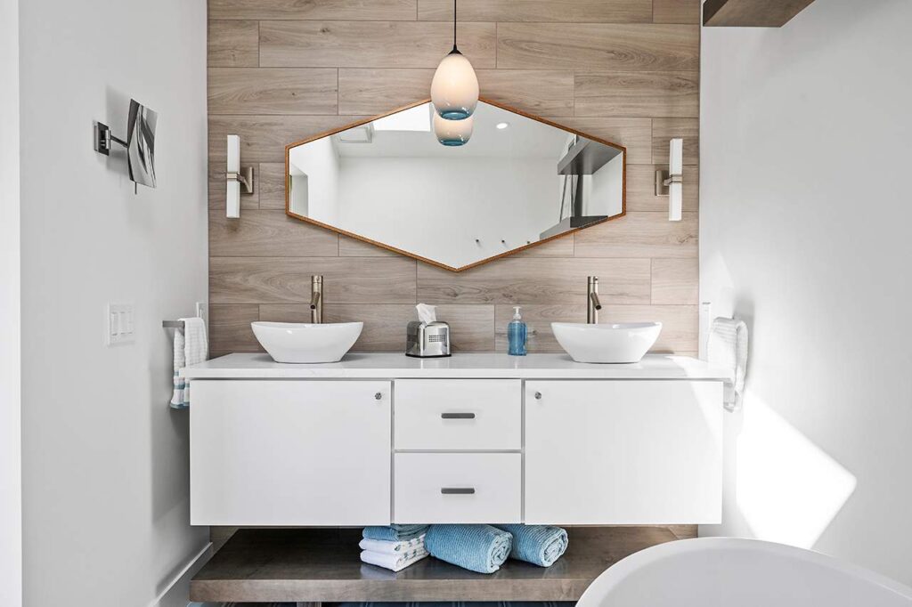 A bright, modern bathroom post-renovation. Features wood accent wall and geometric mirror