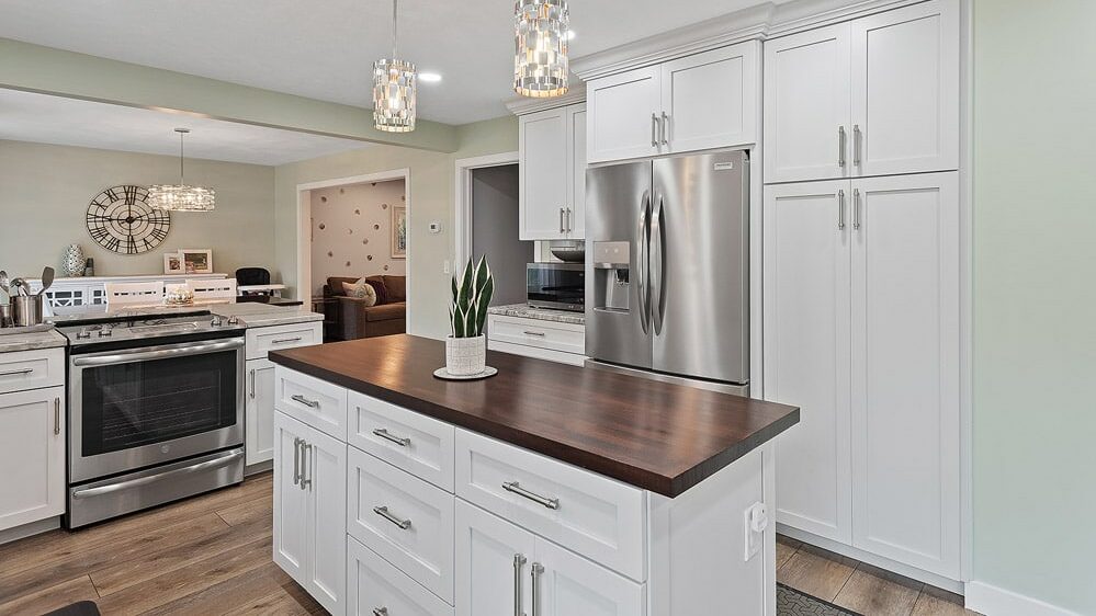 A white kitchen island with wood countertop. Statement lights hang overhead